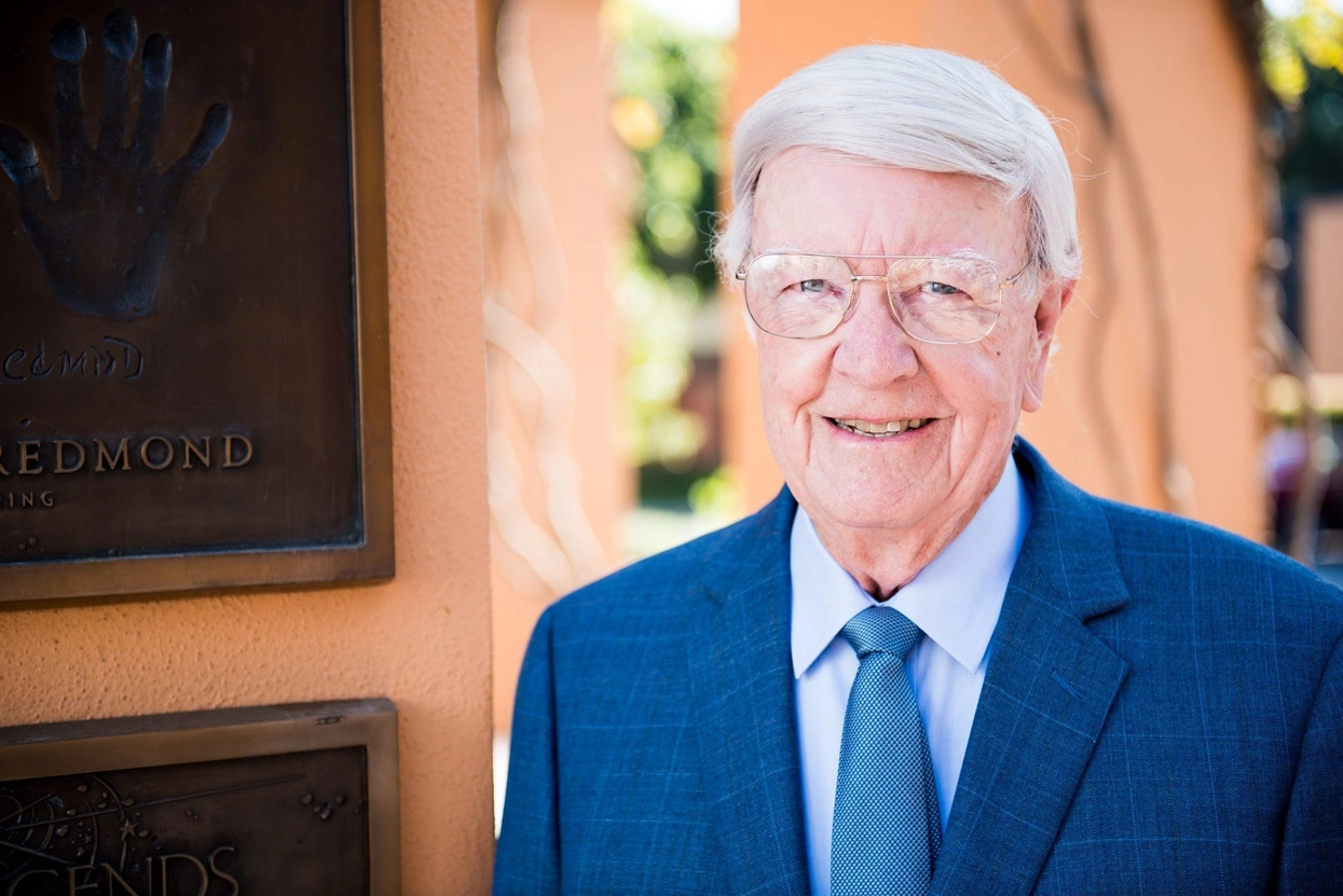 Don Iwerks smiling in a suit beside a handprint plaque