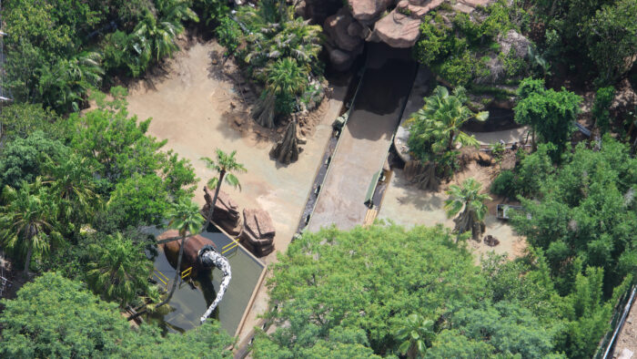 Aerial view of drained Ultrasaur Lagoon at Jurassic Park River Adventure, with a dinosaur animatronic partially reassembled beside the empty ride path